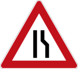 Verkehrszeichen 121-1 „Einseitig verengte Fahrbahn rechts“ mit einem weißen Grund, schwarzem Piktogramm und rotem Rand, das darauf hinweist, dass die Fahrbahn sich von rechts verengt.